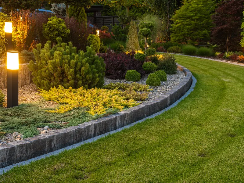 Gepflegte Gartenanlage mit Rasenkante und Beleuchtung im Abendlicht