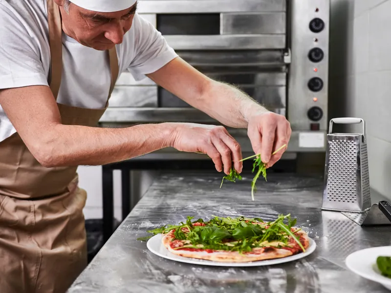 Pizzabäcker belegt eine Pizza mit frischem Rucola