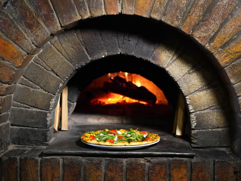 Pizza im brennenden Steinofen aus Ziegeln